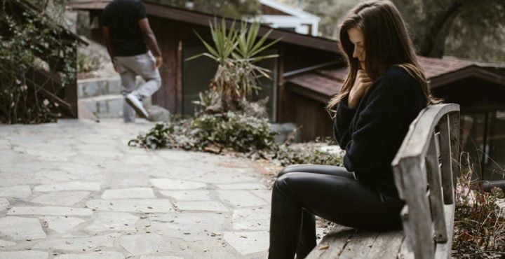 Thoughtful woman sitting on a bench with man working away after divorce